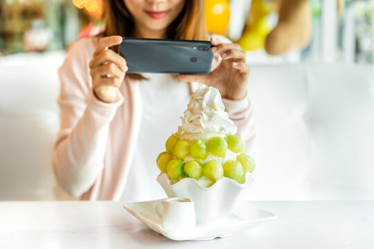 Young woman taking photo of bingsu with smart phone in restaurant and uploading the photos to the social media