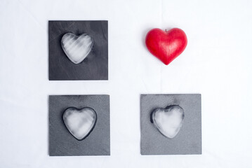 One red love heart, and 3 hearts made of ice placed on 3 slate plates, on a white background. Graphic and geometric, concept of love