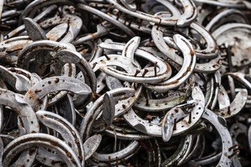 Big pile of large rusty old worn stainless steel silver metal horse shoes and tacks nails removed by farrier and stored in his yard for recycling by blacksmith