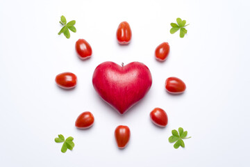 One red love heart, surrounded by small tomatoes and clover leaves, looking like a shining sun or a flower, white background. Concept of love and valentine's day