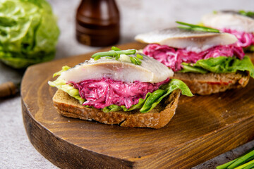 Healthy sandwich with salted herring, beet, and green salad on wooden board. Herring is a saurce of omega 3 fats healthy for brain and mental clarity. Brain food concept. Home cooking