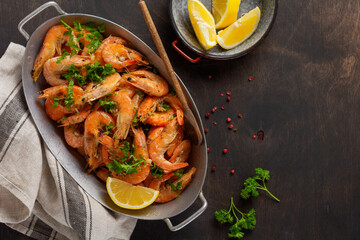 Roasted shrimps with garlic, lemon and parsley, black background, top view, copy space.