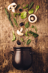 Layout of  fresh vegetables and mushrooms entering in the dark black pot against old wooden kitchen table background with raw texture. Nature spring time for healthy food. Creative concept of vegan