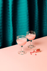 Two glass of wine with creative drink and pills look a like or sweer candy lay on a floor with small bottle against pink background and blue cyan silk fabric.
