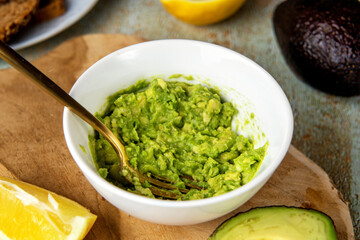 Close up of mashed avocado in a plate with fork on cooking table. Healthy vegan food concept. High saturated fats can help to maintain healthy cholesterol levels. Brain food