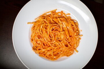 cream spaghetti with tomato sauce in a white porcelain plate. Close up view and black, blurry background.
