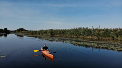 Aerial view of young man floats on an orange kayak on the river. The banks of the river are overgrown with reeds. Ukraine, Europe