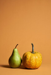 Studio shot of ripe green pear and yellow pumpkin in still life with soft shadows isolated over orange background. Autumn composition of fruits and vegetables for vegetarian menu