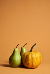 Studio shot of two ripe green pears and yellow pumpkin in still life with soft shadows isolated over orange background. Autumn composition of fruits and vegetables for vegetarian menu