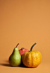 Still life of yellow pumpkin, green pear and red pomegranate isolated over orange background. Autumn composition of fruits and vegetables