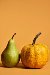 Studio shot of ripe green pear and yellow pumpkin in still life with soft shadows isolated over orange background. Autumn composition of fruits and vegetables for vegetarian menu