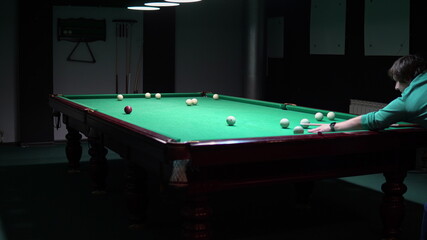 A man plays Russian billiards. aims with the cue and hits the ball