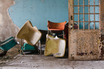 Fototapeta na wymiar Stacks of colored chairs inside an abandoned mental asylum