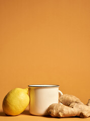 Still life of yellow lemon and ginger root near the mug isolated over orange background. Healthy lifestyle, ingredients for tea concept