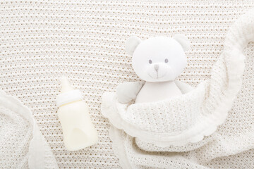 Teddy bear and bottle of milk on light white blanket. Baby feeding concept. Closeup. Top down view.