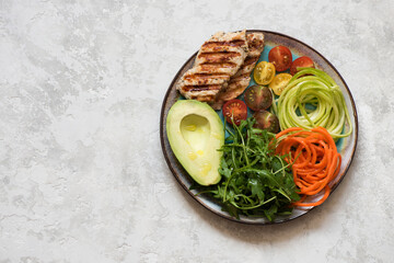Balanced food concept. Salad with grilled chicken breast, arugula, avocado, carrots and zucchini, balanced clean eating, top view. Healhty lunch bowl.