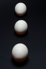 Eggs on a black background, three eggs in a row, shadow on the background of eggs, healthy and diet food.
