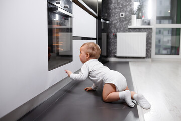 Infant baby boy near oven in home kitchen.