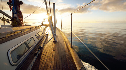 Sloop rigged modern yacht with wooden teak deck sailing at sunrise. A view from the deck to the...