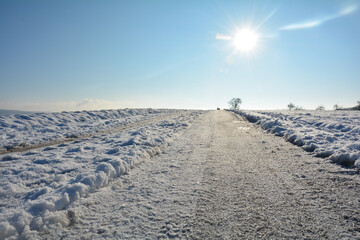 Snow-covered road in the country, with snow in the fields with sky and sun