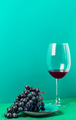 A bunch of blue grapes and a glass of red wine on a bright colored background. Close-up with copy space. Colorful.