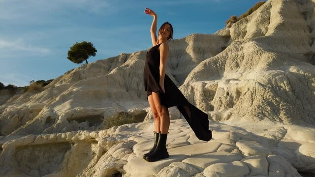 Bella ragazza con vestito nero e stivali nei calanchi