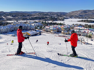 Skiers admiring Mont and Lake Tremblant village resort in winter, Quebec, Canada