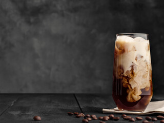 Coffee and milk are mixed in a highball glass with ice. Gray wooden table. Copy space, space for...