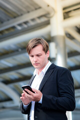 Urban smart caucasian businessman age 30-40 years old In a dark suit standing and using a smartphone To contact and negotiate business outside the office