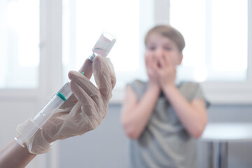 The child looks at the syringe in horror. Fear of injection. Emotions, unwillingness to get vaccinated