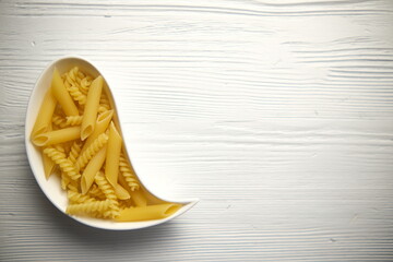 A drop-shaped plate with pasta on a wooden white background. Empty space for the label. The view from the top