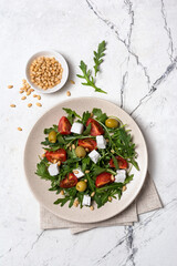 Healthy vegetarian salad with fresh arugula, cherry tomatoes, soft cheese, olives and pine nuts