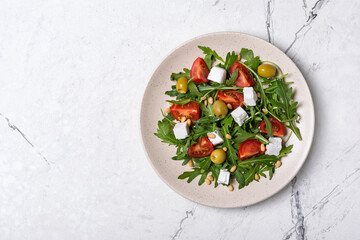 Healthy vegetarian salad with fresh arugula, cherry tomatoes, soft cheese, olives and pine nuts