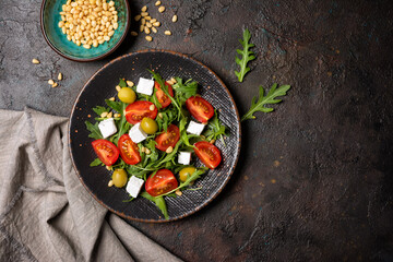 Healthy vegetarian salad with fresh arugula, cherry tomatoes, soft cheese, olives and pine nuts