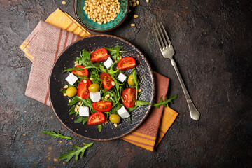 Healthy vegetarian salad with fresh arugula, cherry tomatoes, soft cheese, olives and pine nuts