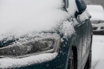 Ein verschneites Auto im Winter. Blick von vorne mit vereisten Scheinwerfern und Motorhaube.