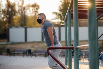 A young man does push-UPS, pull-UPS on a sports field in a mask during a pandemic at sunset. Sports, healthy lifestyle