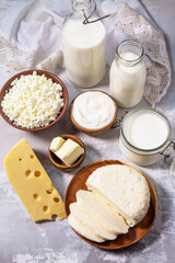 Various fresh dairy products, milk, sour cream, cottage cheese, yogurt and butter on a light stone countertop.