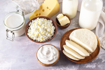 Various fresh dairy products, milk, sour cream, cottage cheese, yogurt and butter on a light stone countertop.