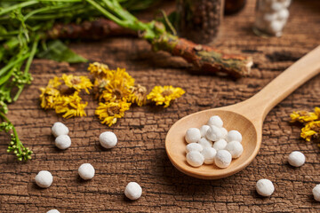 concept of homeopathic pills in a wooden spoon and bottles with herb on wooden table background                                                   