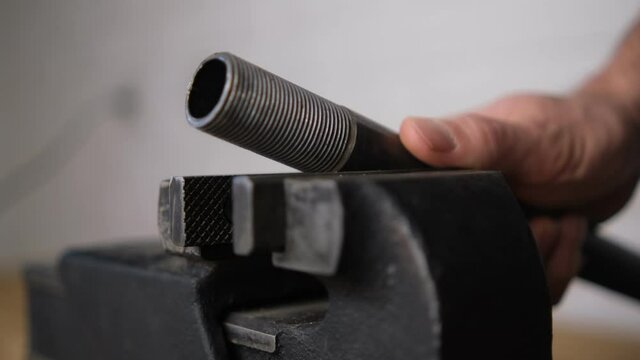 The man unhooked an iron pipe with a carving in a black vise with a screw handle, Close-up, Blurred background. brick background 4k bokeh Flu. Side view.