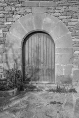 Obraz premium Beautiful wooden medieval door in rustic building with natural stones arch.Black and white photo.