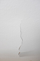 A crack in the white plastered ceiling. Concept of dilapidated housing and poor repair. vertical photo