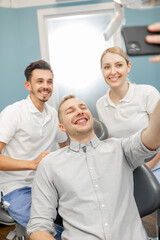 Young male patient in dental braces making selfie photo with a dentist and assistant during a regular orthodontic visit at the dental office. Happy dental appointment concept. High quality photo