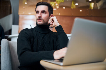 Handsome young businessman working online on laptop indoors