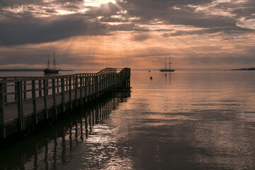 Obraz premium Silhouette of pier and sailing ships with epic sunburst.