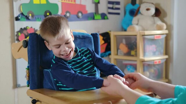 Activities for kids with disabilities. Preschool Activities for Children with Special Needs. Mom is playing with Boy with Cerebral Palsy in special chair at home