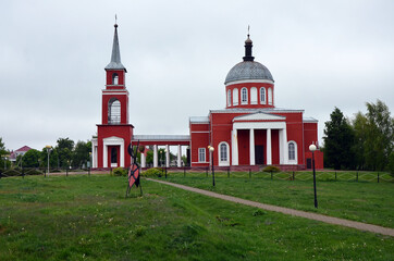 Orthodox church in dark red on a green field against the background of the forest