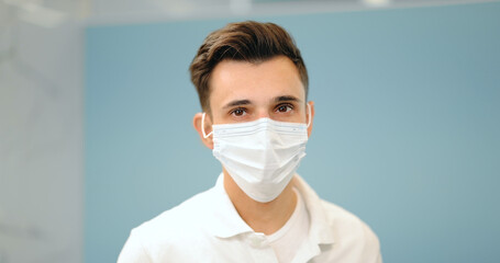 Portrait of a young smiling dentist turkish ethnicity wearing facial mask. Portrait of a male medic on a blue background. 4k video screenshot, please use in small size