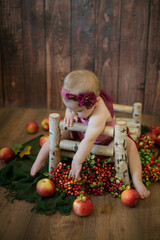 Fototapeta na wymiar Little sweet girl up to one year old in a beautiful burgundy velvet suit with red juicy apples on a crib made of wood. Healthy lifestyle 